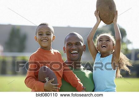 Stock Image - African American father, son and daughter playing football. Fotosearch
