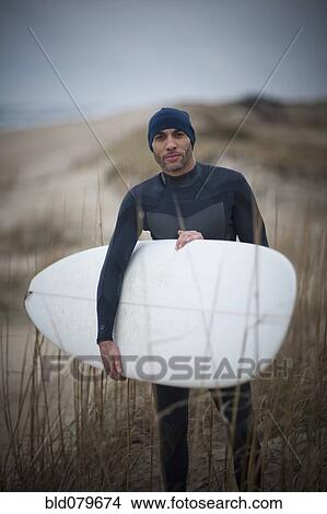Picture - African American man in wet suit carrying surfboard. Fotosearch