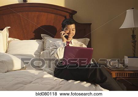 Stock Photo - Chinese businessman using laptop in hotel room. Fotosearch