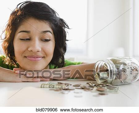 Stock Photograph - Hispanic woman looking at change in glass jar. Fotosearch