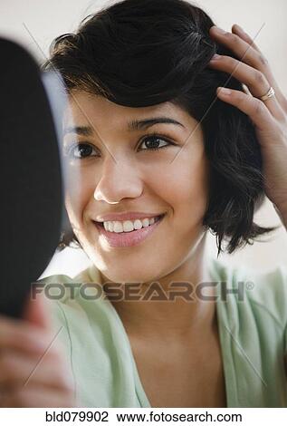 Stock Image - Hispanic woman looking at hair in mirror. Fotosearch