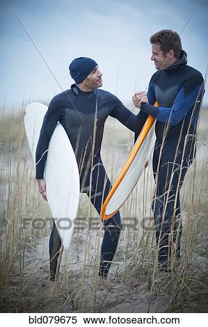Stock Photography - Men wearing wetsuits and carrying surfboards. Fotosearch