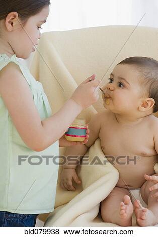 Stock Photo - Mixed race girl feeding baby brother. Fotosearch