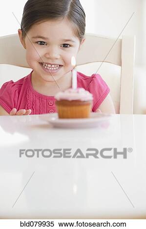 Stock Photography - Mixed race girl looking at birthday cupcake. Fotosearch