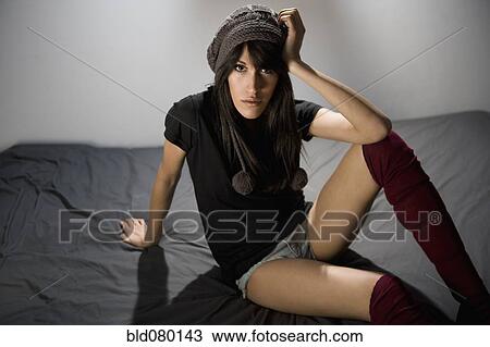 Stock Image - Serious mixed race woman sitting on bed. Fotosearch