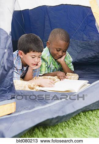 Stock Image - Boys reading book in tent. Fotosearch
