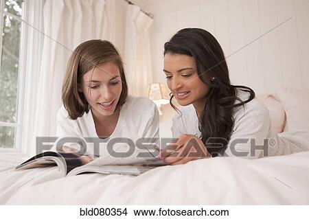 Friends laying on bed looking at magazine View Large Photo Image Picture - Friends laying on bed looking at magazine. Fotosearch