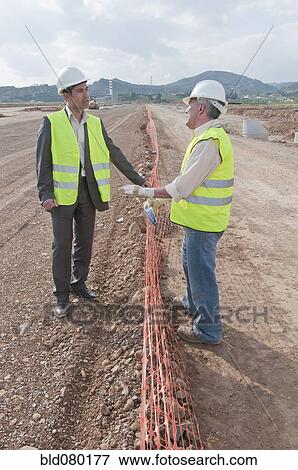 Stock Photo - Hispanic businessman and construction worker standing in field. Fotosearch