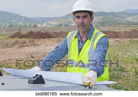Stock Photography - Hispanic construction worker in field with blueprints. Fotosearch