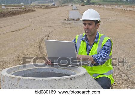 Stock Photo - Hispanic construction worker using laptop in field. Fotosearch