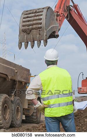 Stock Photo - Hispanic construction worker watching backhoe. Fotosearch