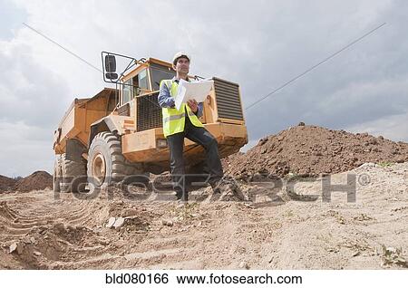Stock Photograph - Hispanic construction worker with blueprints near dump truck. Fotosearch