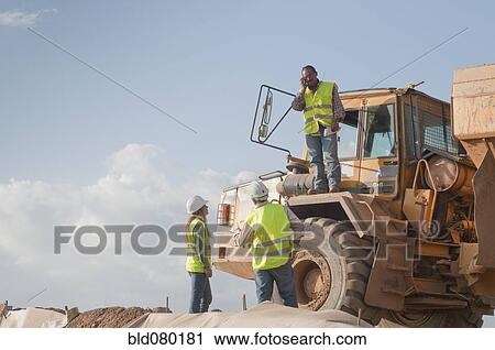 Stock Image - Hispanic construction workers near dump truck. Fotosearch