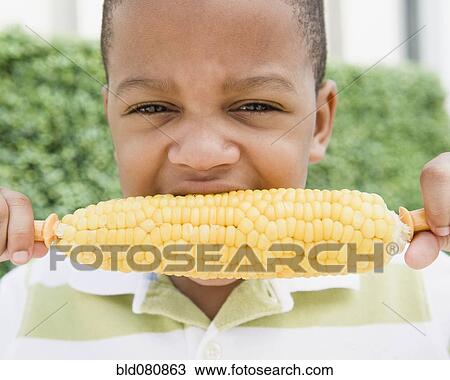 Stock Image - African American boy eating corn on the cob. Fotosearch