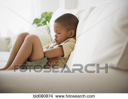 Picture - African American boy unhappy on sofa. Fotosearch