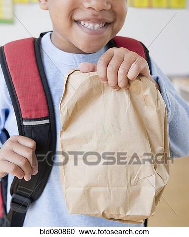 Stock Image - African American boy wearing backpack holding bag lunch. Fotosearch
