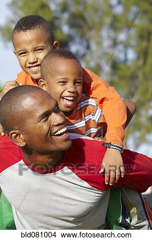Picture - African American father giving sons piggy back ride. Fotosearch