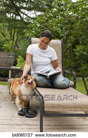 Stock Photo - African American woman reading book and petting dog. Fotosearch