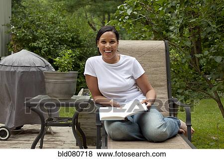 Stock Photo - African American woman reading book in back yard. Fotosearch