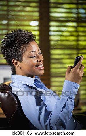 Stock Photography - Black businesswoman in office text messaging. Fotosearch