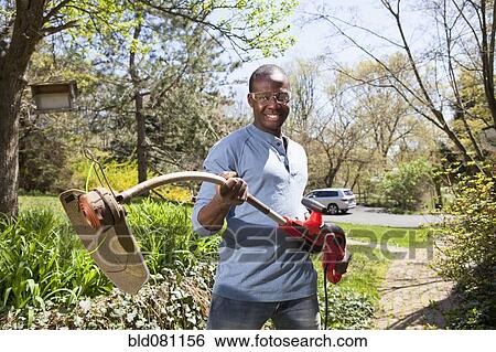 Stock Photograph - Black man holding weed trimmer. Fotosearch