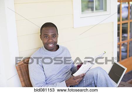 Stock Image - Black man on porch reading magazine. Fotosearch