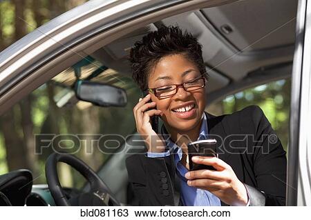 Stock Image - Black woman in vehicle using two cell phones. Fotosearch