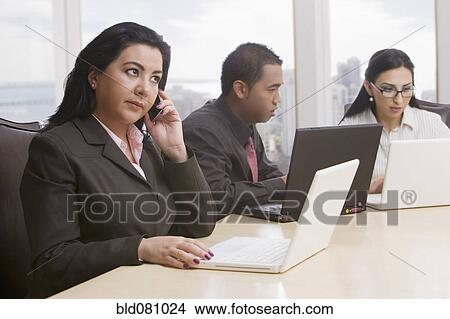 Picture - Business people in meeting using cell phone and laptops. Fotosearch