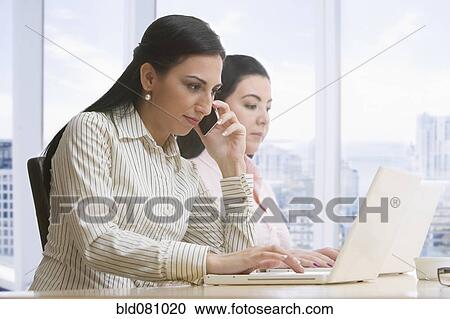 Stock Image - Businesswomen using laptops and cell phone. Fotosearch
