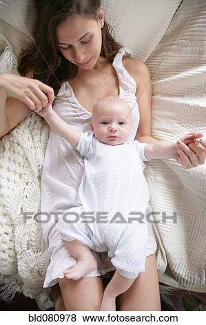 Stock Photo - Caucasian mother laying on bed with baby. Fotosearch