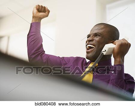 Stock Photo - Cheering Black businessman holding telephone. Fotosearch