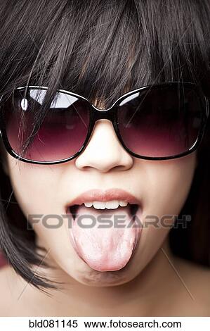 Stock Photography - Chinese woman wearing sunglasses and tongue out. Fotosearch