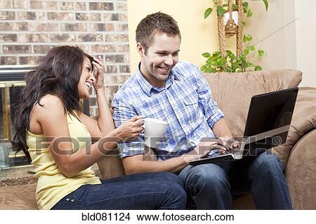 Couple sitting in living room using laptop View Large Photo Image Picture - Couple sitting in living room using laptop. Fotosearch