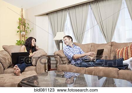 Stock Image - Couple sitting in living room using laptops. Fotosearch