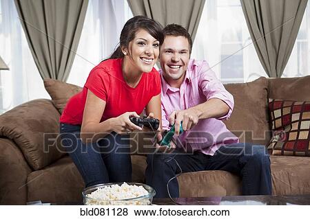 Couple sitting on sofa and playing video game View Large Photo Image Stock Photo - Couple sitting on sofa and playing video game. Fotosearch