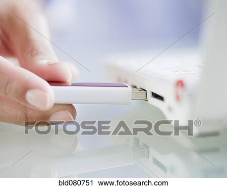 Stock Image - Hand pushing USB stick into laptop. Fotosearch
