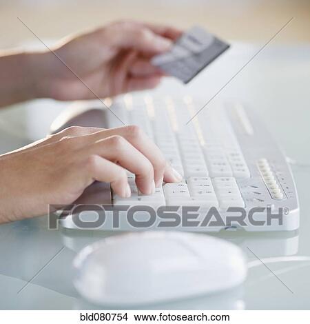 Picture - Hands holding credit card while typing on computer keyboard. Fotosearch