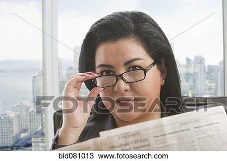 Stock Image - Hispanic businesswoman reading newspaper in office. Fotosearch