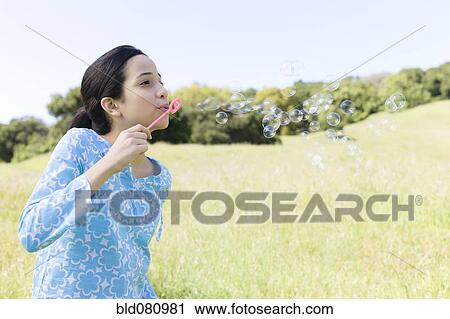 Stock Image - Hispanic girl blowing bubbles in field. Fotosearch