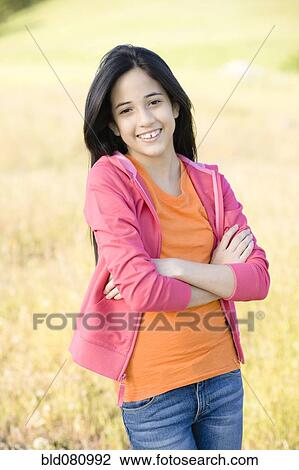 Stock Image - Hispanic girl in field with arms crossed. Fotosearch