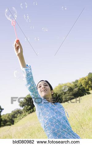 Stock Image - Hispanic girl making bubbles in field. Fotosearch
