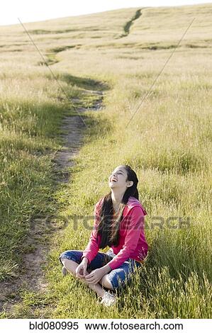 Stock Photography - Hispanic girl sitting in field laughing. Fotosearch