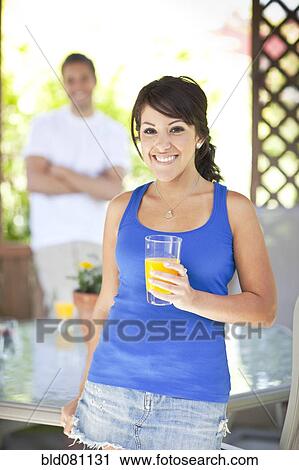 Stock Image - Hispanic woman drinking orange juice on patio. Fotosearch