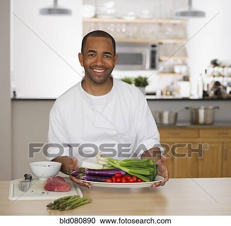 Stock Image - Mixed race chef holding plate of vegetables. Fotosearch