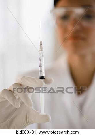 Stock Image - Mixed race doctor holding syringe. Fotosearch