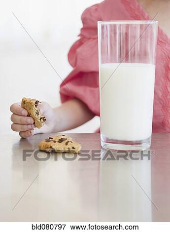 Stock Photo - Mixed race girl eating cookie with glass of milk. Fotosearch