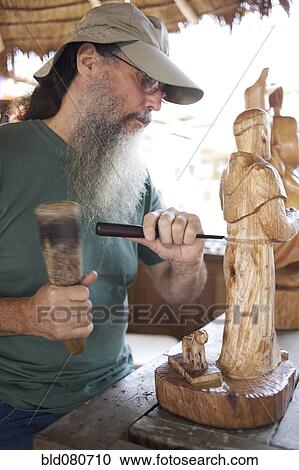 Stock Image - Mixed race man carving wooden statue. Fotosearch