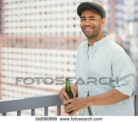 Stock Photo - Mixed race man drinking beer near railing. Fotosearch