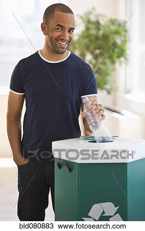 Stock Image - Mixed race man putting plastic bottle in recycling bin. Fotosearch