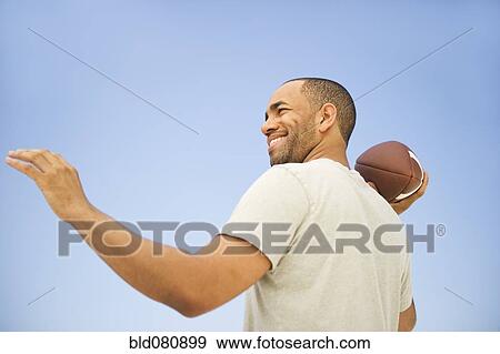 Stock Photo - Mixed race man throwing football. Fotosearch